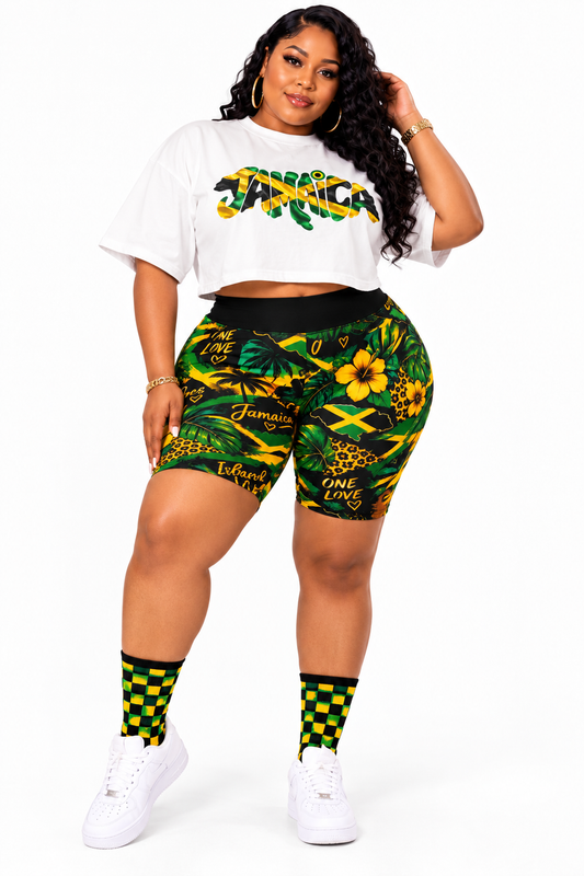A plus-size model wearing Jamaica-themed athletic wear, featuring a white crop top with a green and yellow graphic, matching green and yellow patterned biker shorts, green and yellow checkered socks, and white sneakers, set against a plain white background.