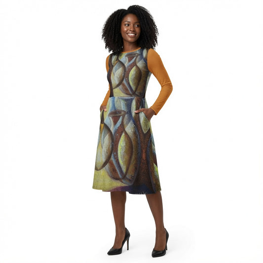A woman modeling a sleeveless A-line dress with a colorful abstract geometric print, layered over a mustard yellow long-sleeve top, against a plain white background.