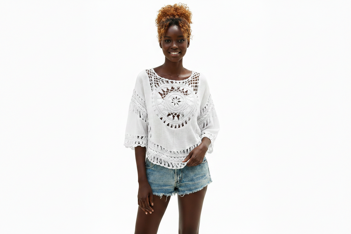 A woman modeling a white crochet lace top with three-quarter sleeves and denim shorts against a plain white background.