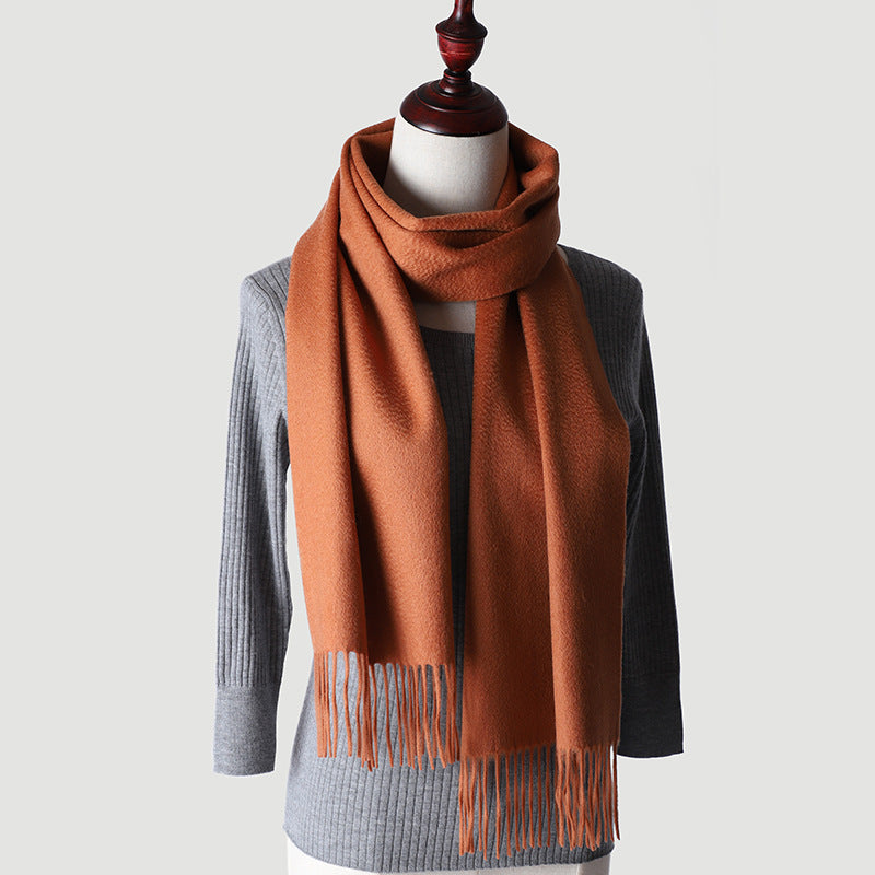 An orange cashmere scarf with a solid color pattern, displayed on a mannequin wearing a grey sweater.
