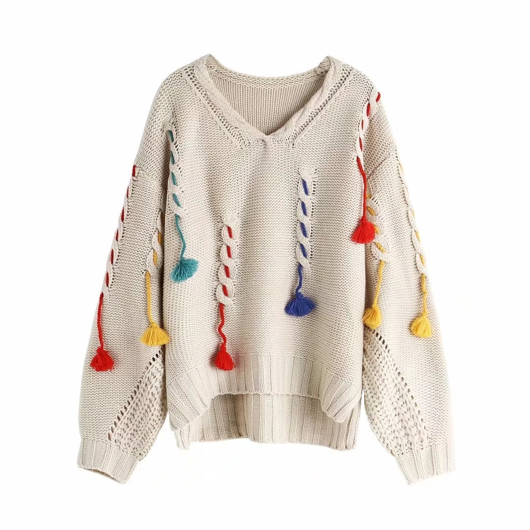 A knitted sweater with colorful tassels hanging from the sleeves, primarily in beige with colorful accents.