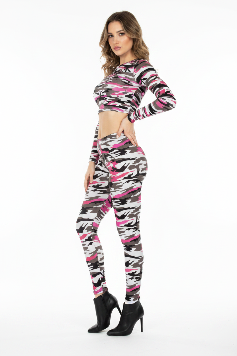 A woman modeling a matching two-piece activewear set featuring a pink, black, and white camouflage pattern, consisting of a long-sleeve crop top and high-waisted leggings, paired with black high-heeled boots against a plain white background.