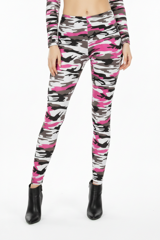 A woman modeling a matching two-piece activewear set featuring a pink, black, and white camouflage pattern, consisting of a long-sleeve crop top and high-waisted leggings, paired with black ankle boots against a plain white studio background.