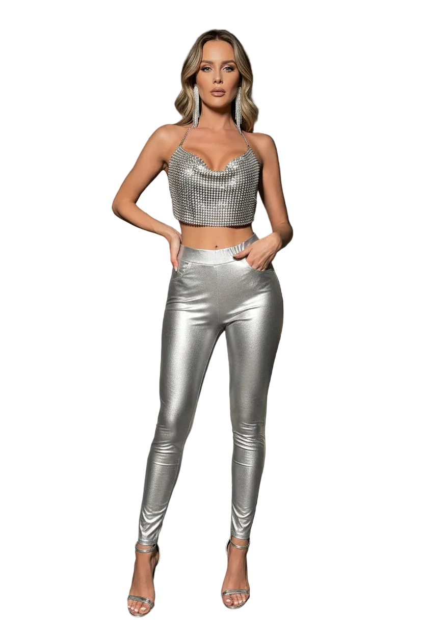 A woman modeling a metallic silver two-piece outfit consisting of a halter crop top and matching high-waisted leggings, paired with silver high-heeled sandals, set against a plain white background.