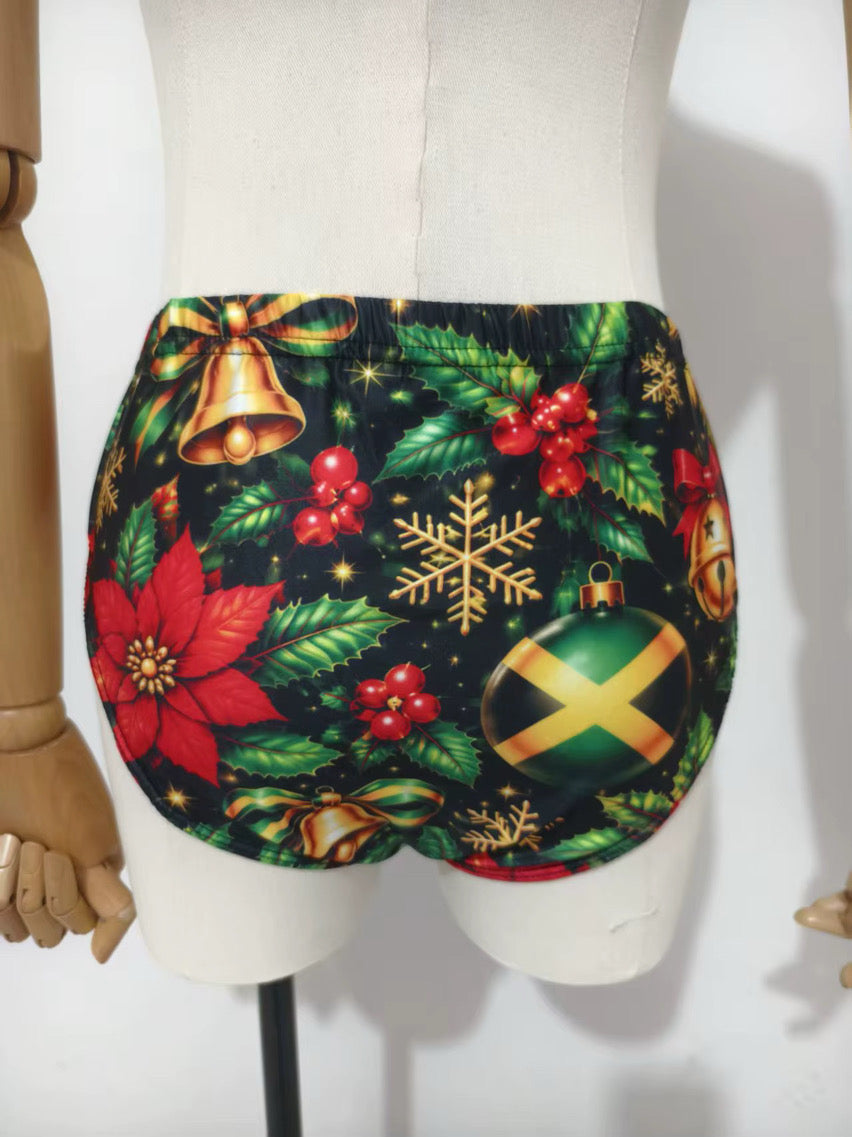 A pair of high-waisted, low-rise bikini bottoms with a vibrant Christmas print featuring green holly leaves, red poinsettias, gold bells and ornaments, displayed on a beige mannequin torso.