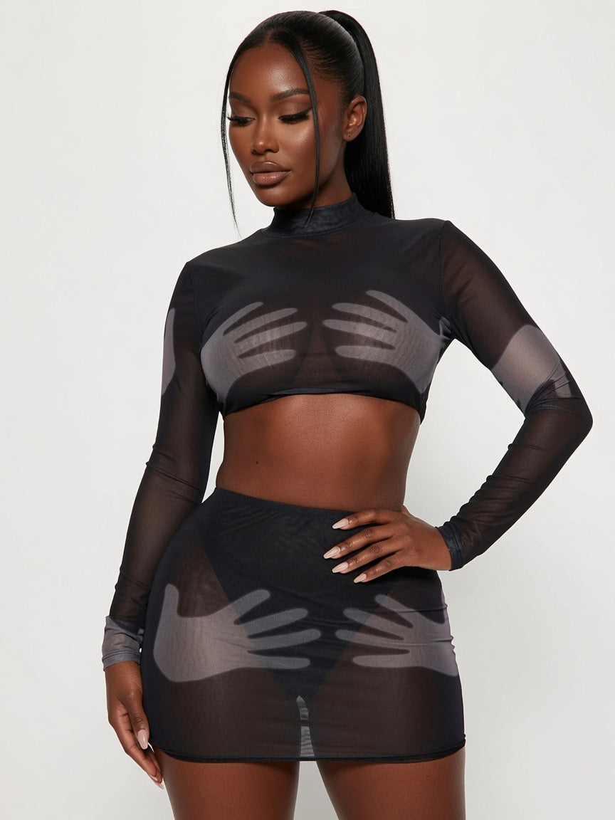 Model wearing a black sheer outfit with long sleeves and a skirt on a white background
