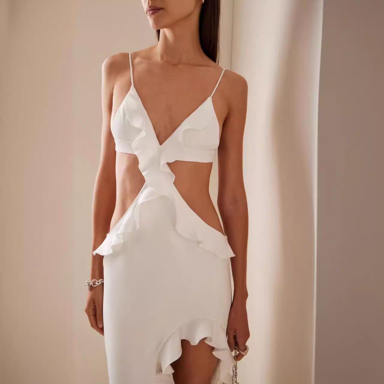 Woman wearing a white dress with a deep neckline and ruffled hem against a neutral background